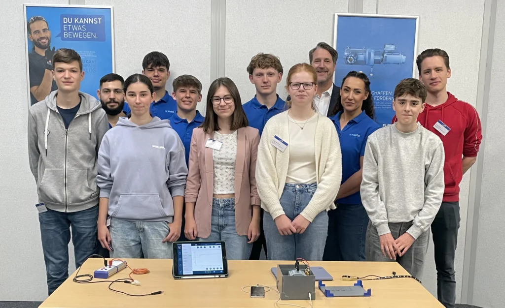 Gruppe von Teilnehmenden der Aktion Schüler macht MINT vor Rollbannern und einem Experimentiertisch