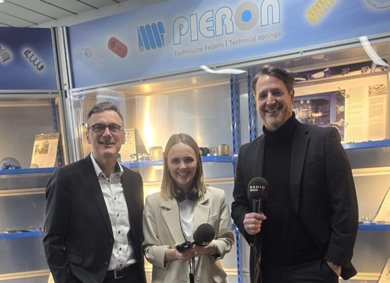 Three people with a microphone in front of a display case with springs and the Pieron lettering